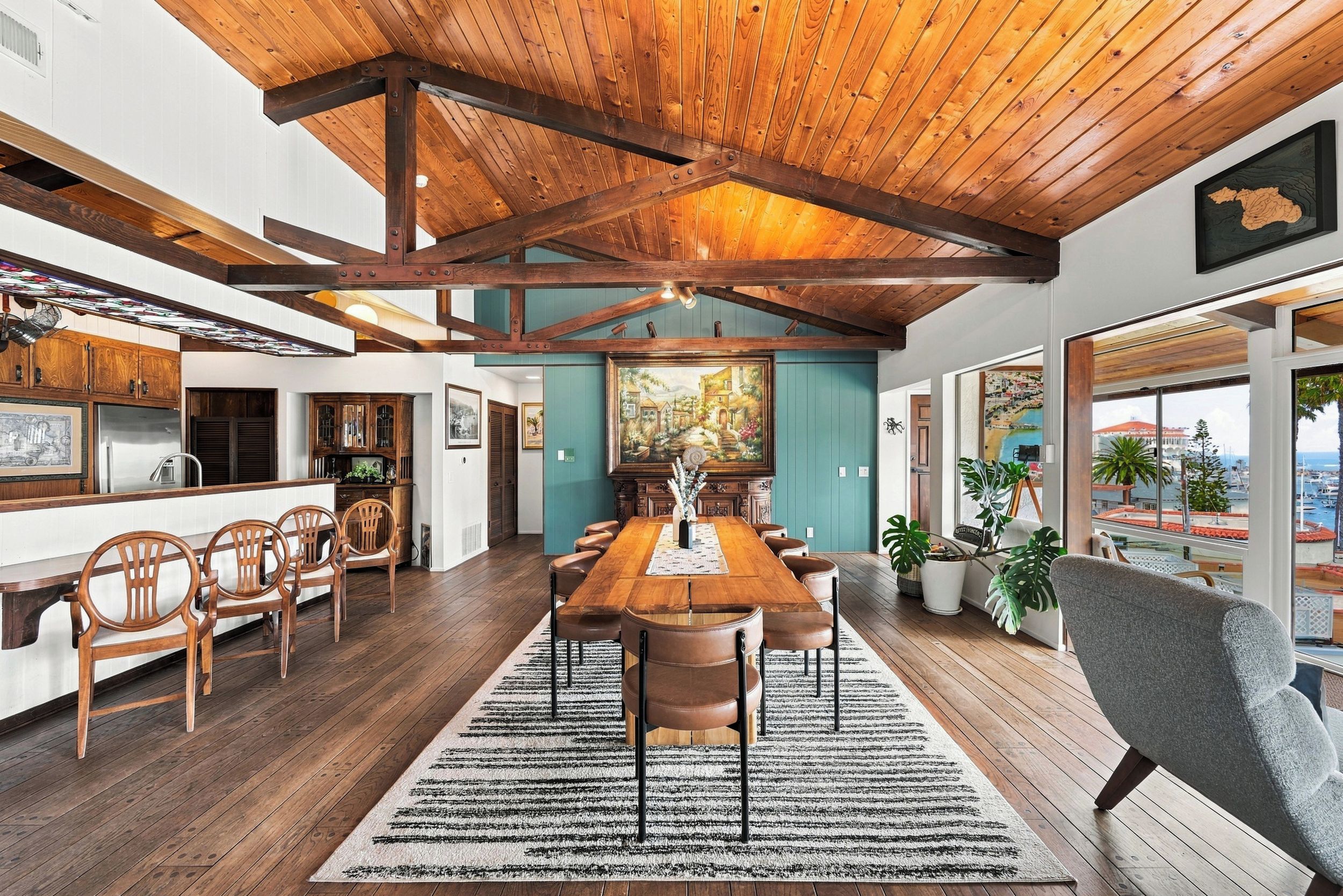 A spacious dining area with a wooden table and chairs, a large painting on the wall, and a view of the sea through the windows.