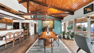 A spacious dining area with a wooden table and chairs, a large painting on the wall, and a view of the sea through the windows.