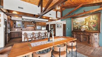 A spacious dining area with a wooden table and chairs, a kitchen in the background, and a large painting on the wall.
