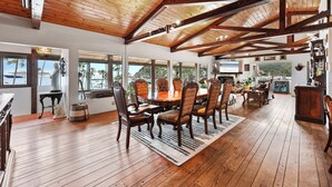 A spacious dining area with a wooden ceiling and large windows offering views of palm trees and a mountain. - Catalina Courtyard Suites (Avalon)