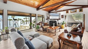 A spacious living room with a wooden ceiling, large windows, and a fireplace. - Catalina Courtyard Suites (Avalon)
