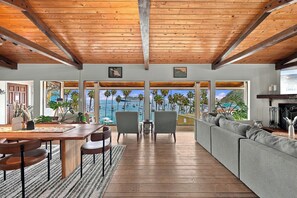 A spacious living area with a wooden ceiling, large windows offering a view of the sea, and a cozy seating arrangement. - Catalina Courtyard Suites (Avalon)