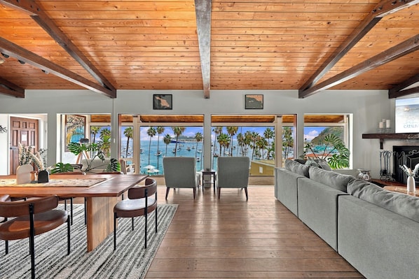 Un espacio habitable amplio con techo de madera, ventanas grandes que ofrecen vista al mar y un rincón de estar acogedor.
