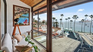 A room with a large window overlooking a marina with boats and palm trees. - Catalina Courtyard Suites (Avalon)