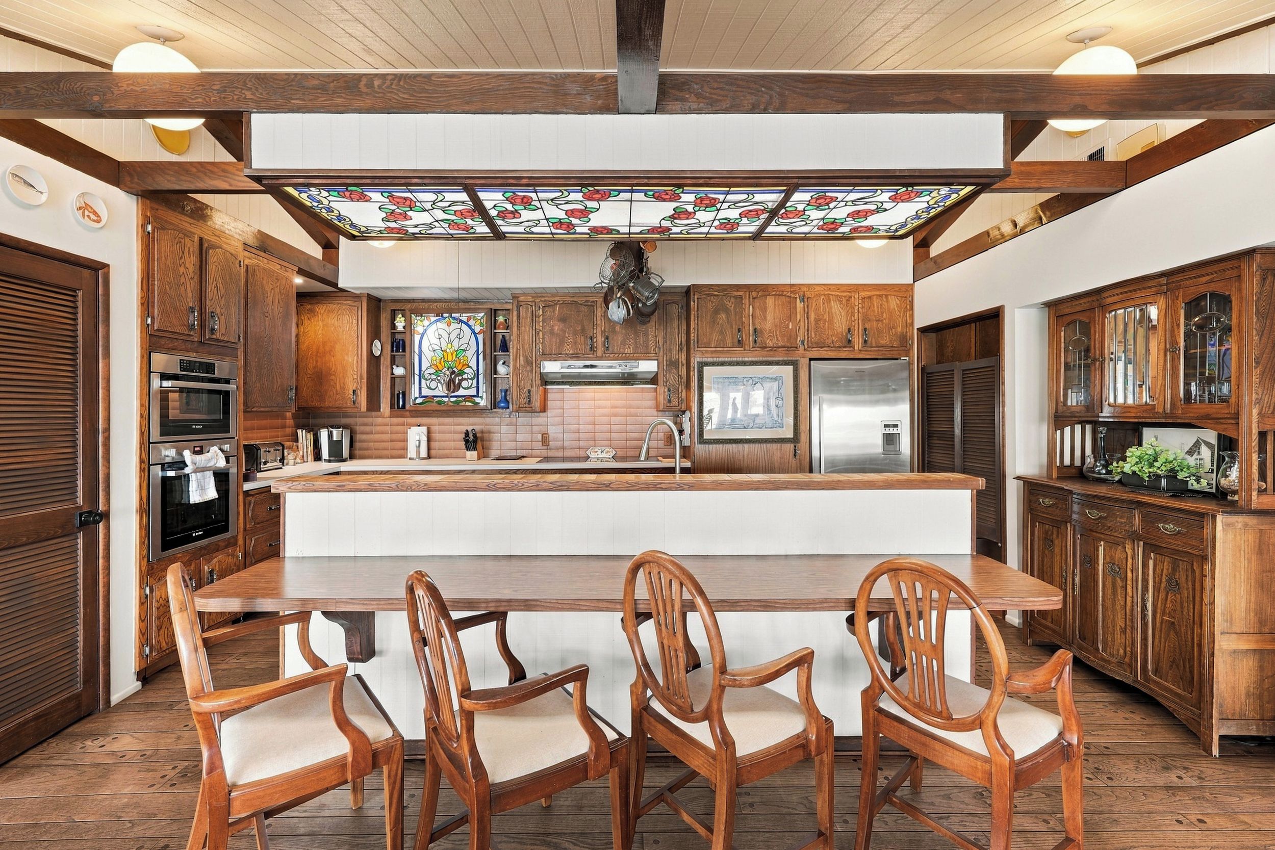 A spacious kitchen with wooden cabinetry, a central island, and a stained glass ceiling.