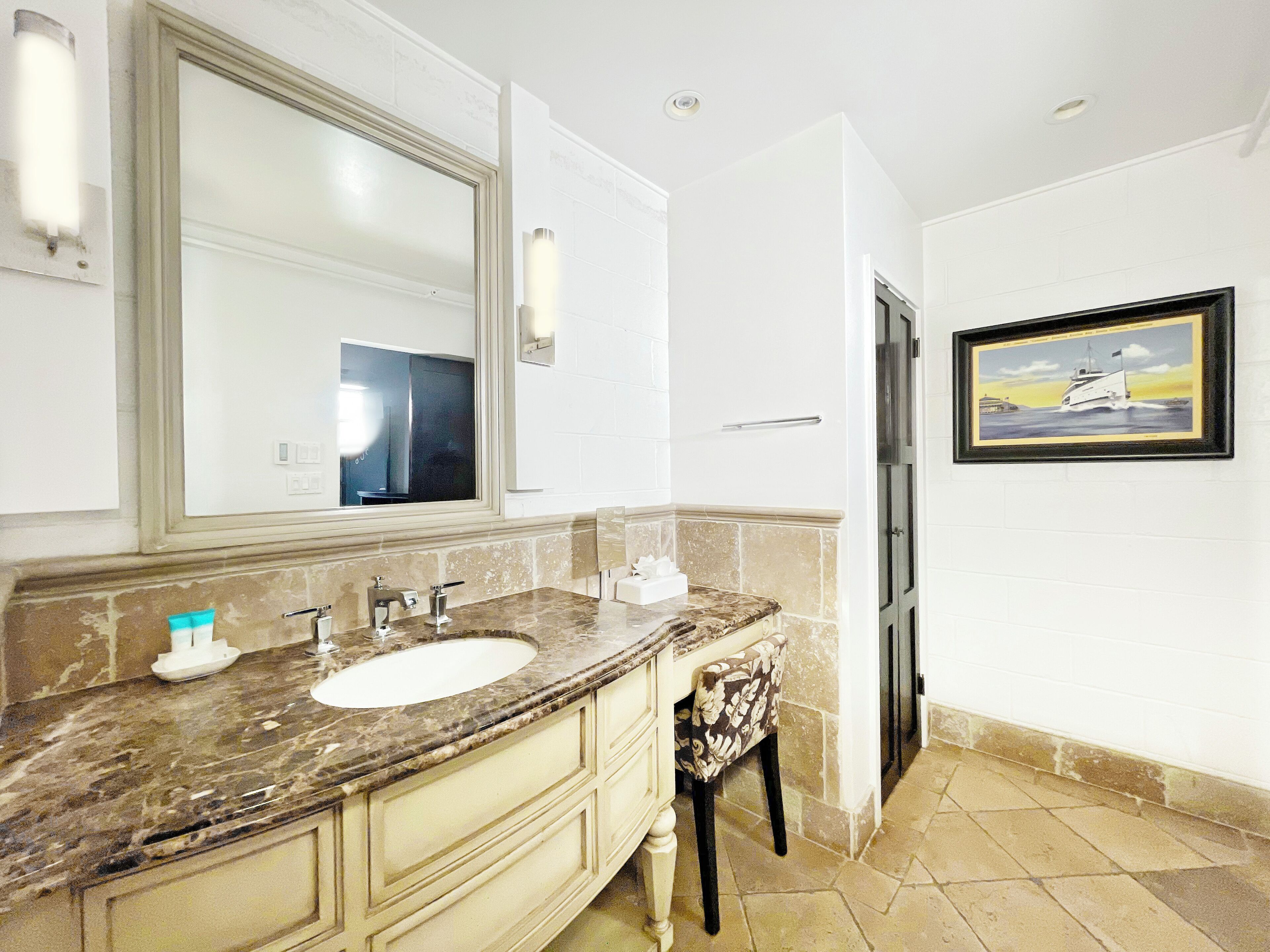 A bathroom with a large mirror, a sink, and a chair.
