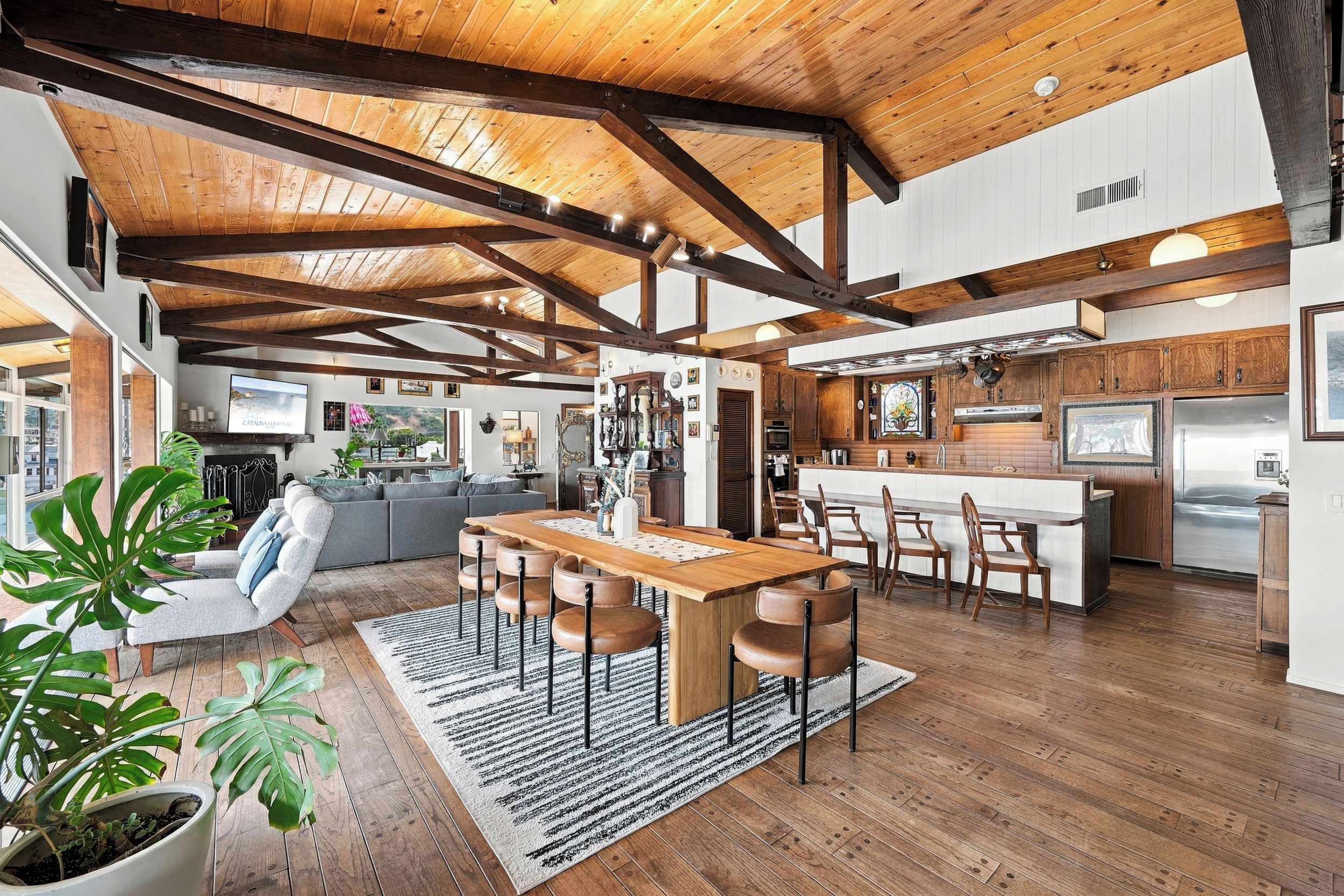 Un vaste espace de vie doté d’un plafond en bois, d’une table à manger avec des chaises et d’une cuisine avec des meubles et des appareils électroménagers en bois.