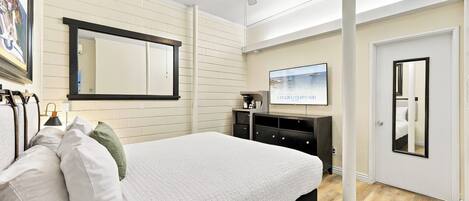 Habitación de hotel con cama, ventilador de techo, televisor de pantalla plana, un espejo grande y una puerta.