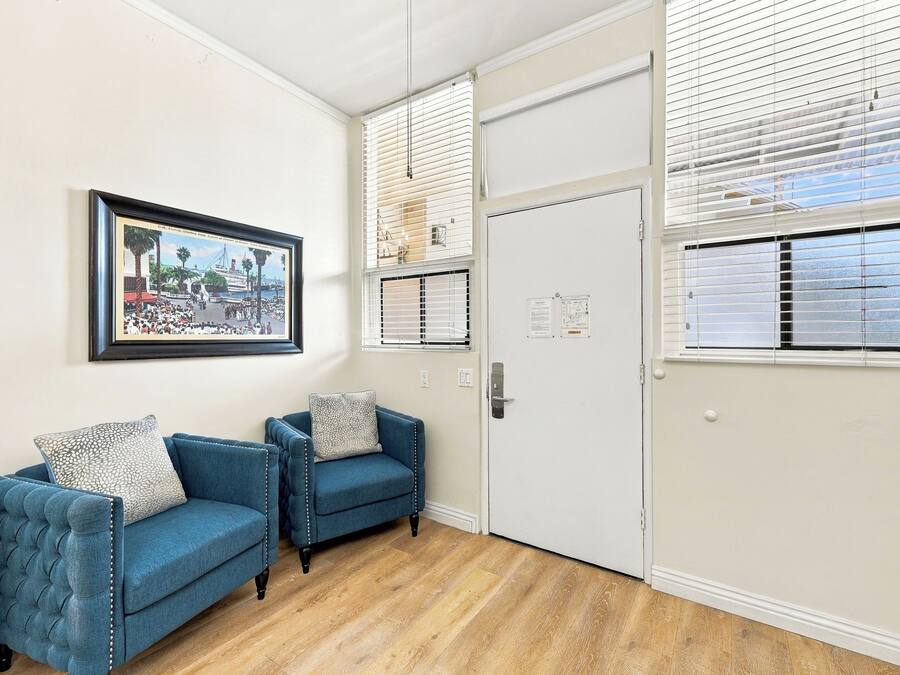 Une pièce avec deux fauteuils bleus, un tableau encadré au mur et une porte blanche sur laquelle est fixé un tableau d’affichage.