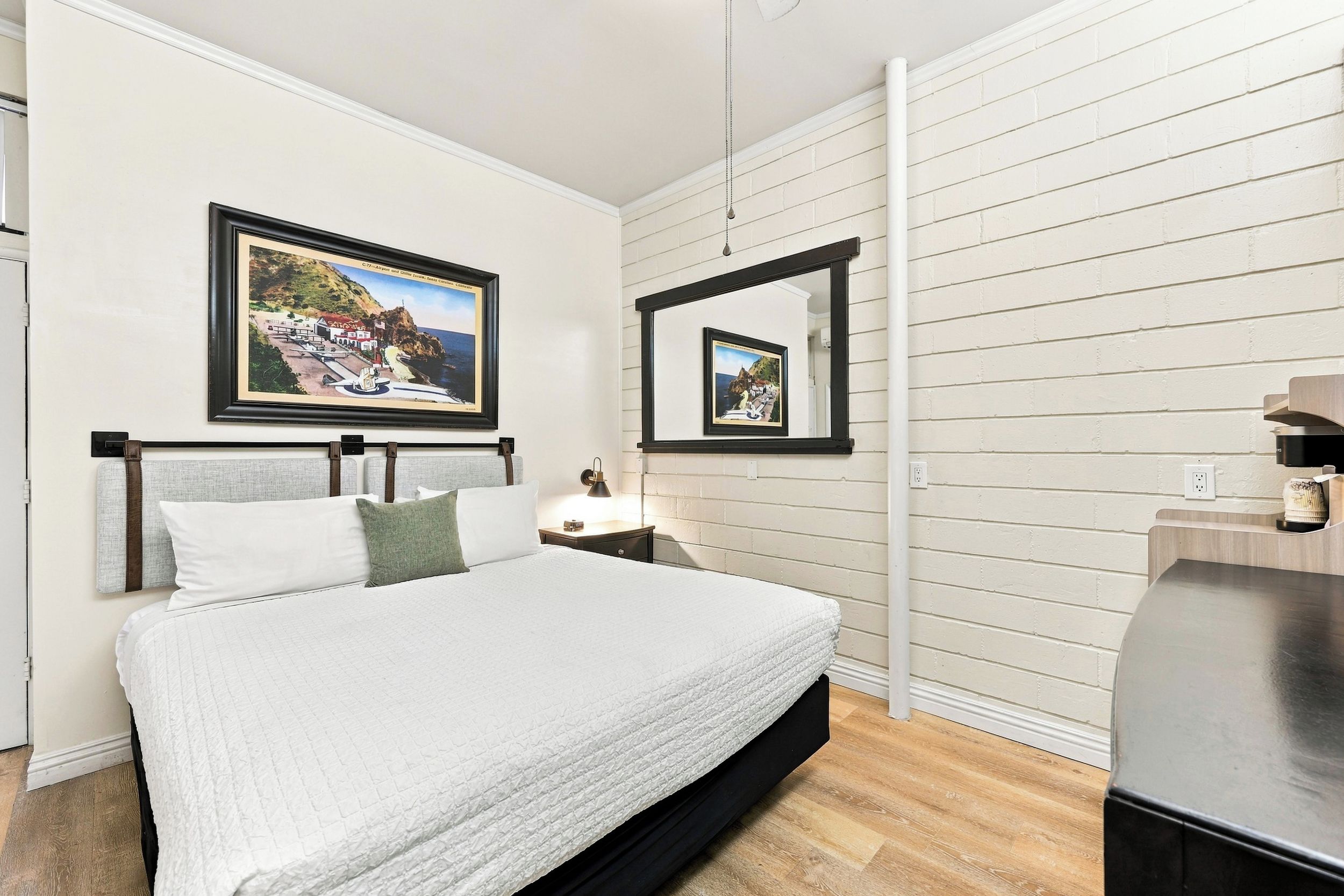 Un dormitorio con una cama, una mesita de noche, una lámpara, un tocador y dos cuadros enmarcados en la pared.