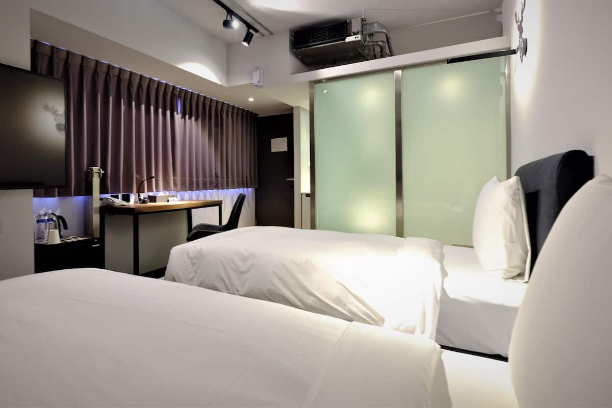 A hotel room with two beds, a desk with a chair, a wardrobe, and a minibar.