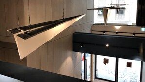 A modern interior with a suspended geometric light fixture and a view of the outside through a large window. - iNN Hotel (Taichung)