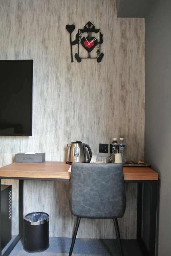 A modern room with a wooden desk, a grey chair, a wall-mounted clock, a television, a kettle, a phone, and a trash bin. - iNN Hotel (Taichung)