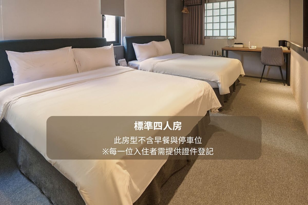 A standard four-room hotel room with two beds, a desk, and a chair.