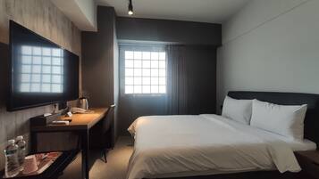 A hotel room with a bed, a desk, a TV, and a window with curtains.
