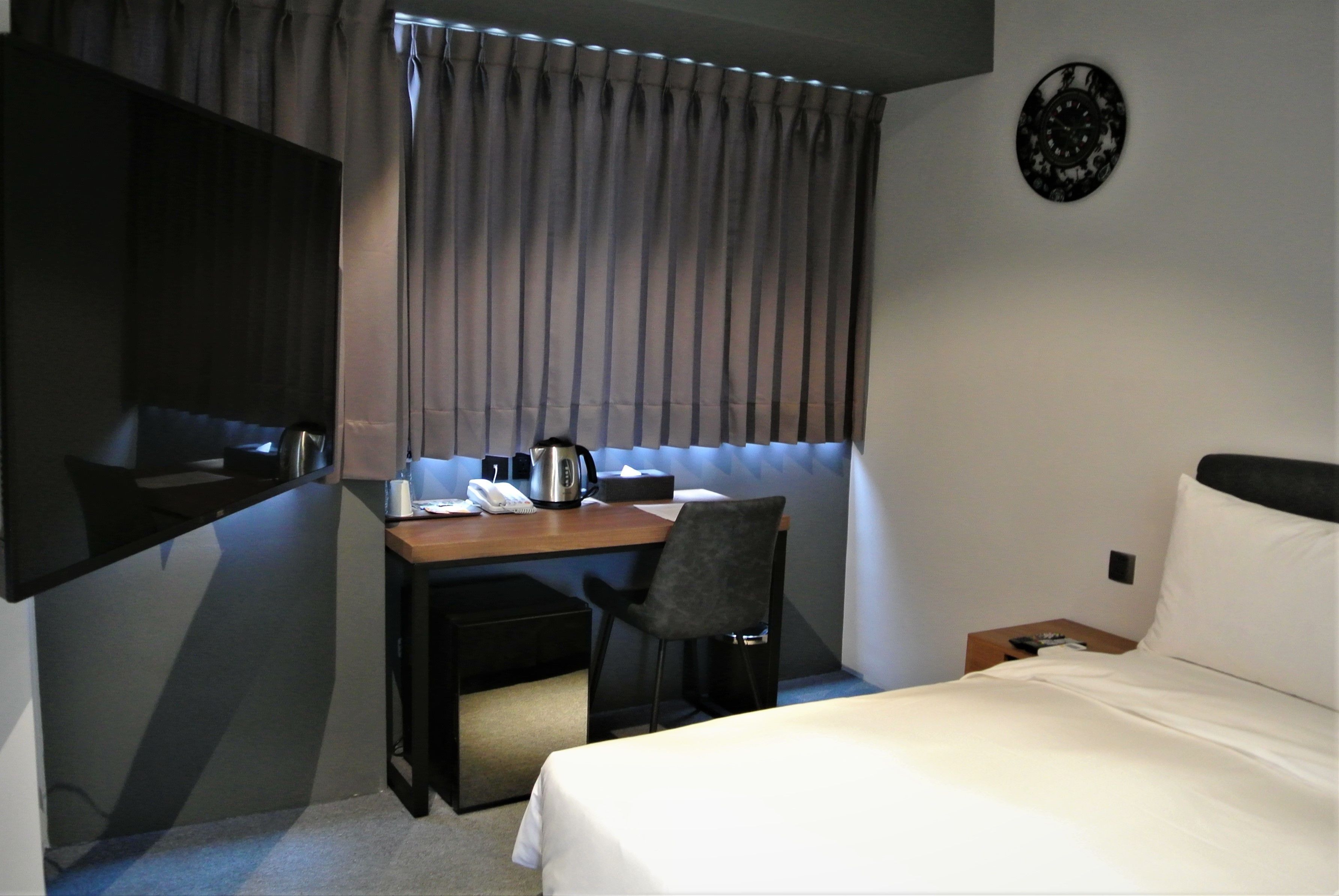 A hotel room with a bed, a desk with a chair, a coffee maker, and a telephone.