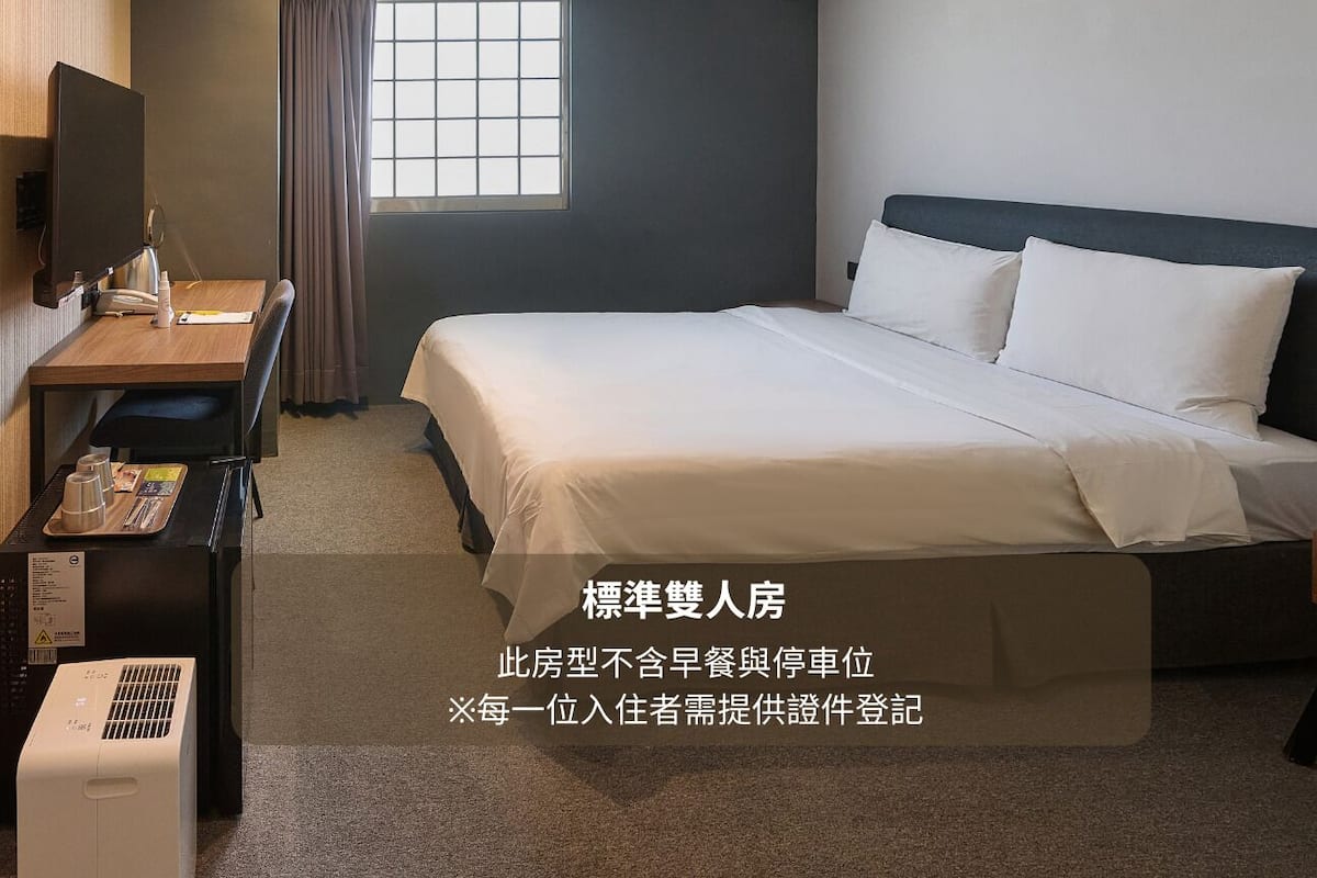 A hotel room with a bed, a desk, a chair, a TV, and a window with curtains.