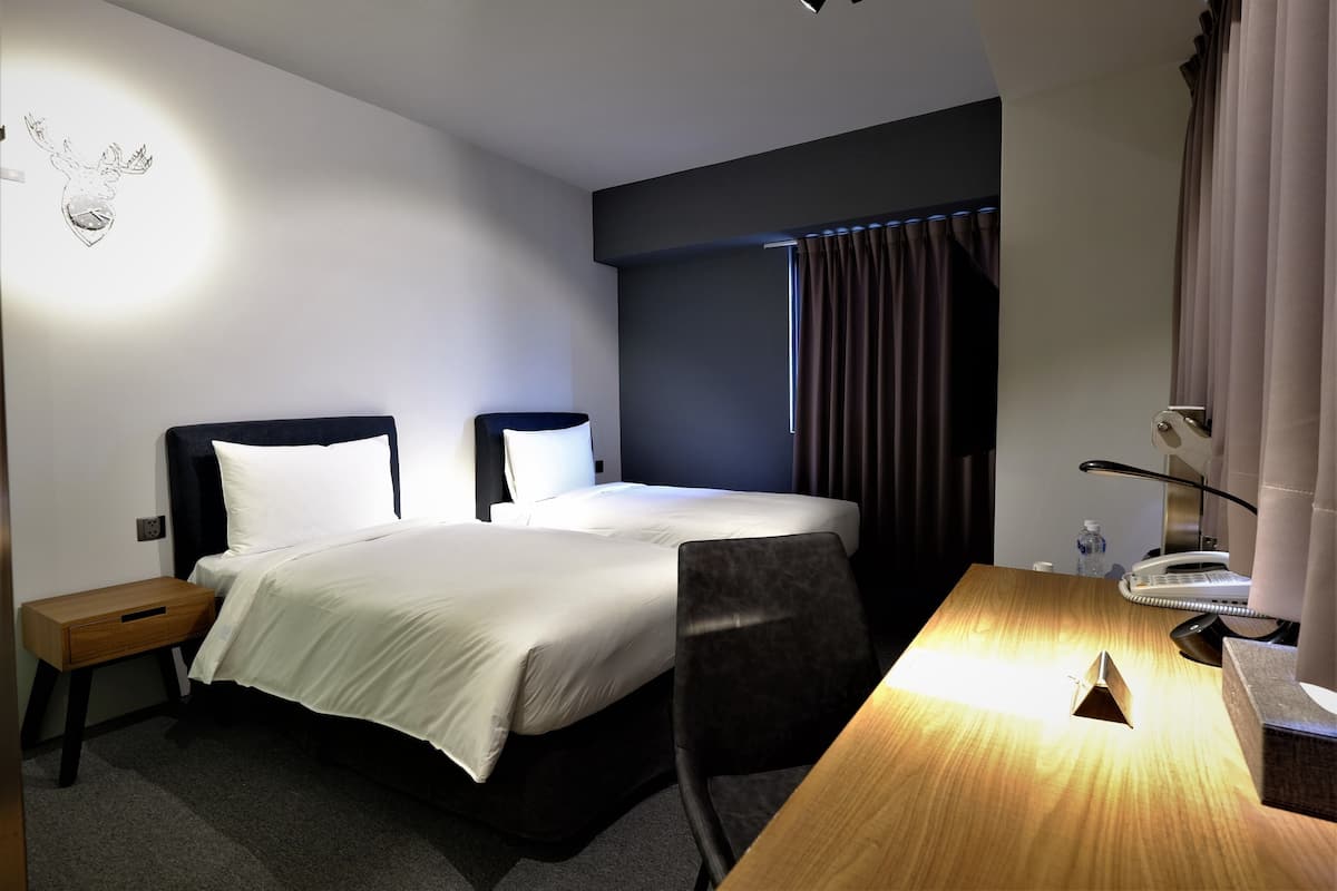 A hotel room with a bed, bedside tables, a desk with a lamp, a chair, and a wall-mounted artwork.