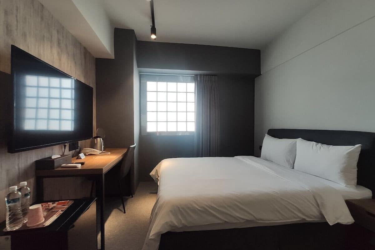 A hotel room with a bed, a desk, a TV, and a window with curtains.