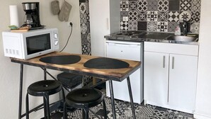 Kompakti keittiö, jossa on mikroaaltouuni, liesi ja seinälle ripustettavat uunikintaat.