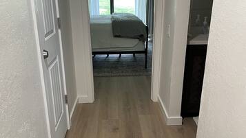 A hallway leading to a bedroom with a bed, a radiator, and a view of a garden through a window.