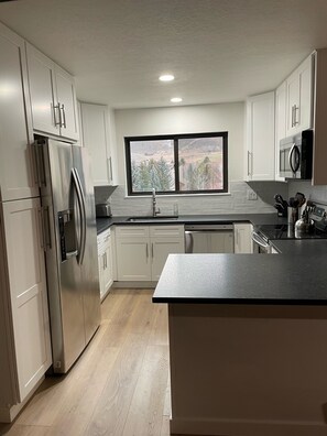 Una cucina moderna con elettrodomestici in acciaio inossidabile, mobili bianchi e un'ampia finestra con vista sull'esterno.