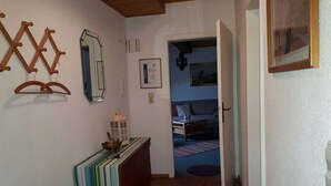 Un couloir avec un banc en bois, des livres, une lanterne et une porte donnant sur une chambre à coucher.