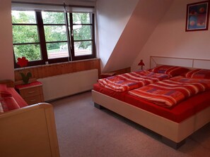 A bedroom with a large bed, a window, a radiator, and a small table with a flower.