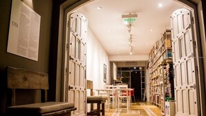 Un pasillo con un banco, puertas abiertas que dan a una habitación y una estantería llena de libros.