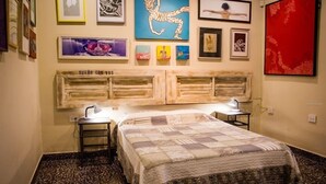 Un dormitorio con una cama, dos mesitas de noche, un cabecero y obras de arte en las paredes.