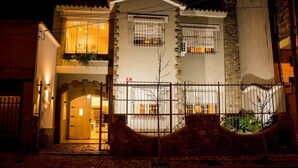 Una casa de dos pisos con entrada protegida por una reja, un balcón con plantas y una ventana con mosquitero de seguridad.