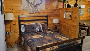 A wooden-paneled room with a bed, a ceiling fan, a lamp, and a small table with a plant.