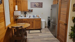 A compact kitchen with wooden cabinets, a microwave, a refrigerator, and a dining area with a table and chairs.