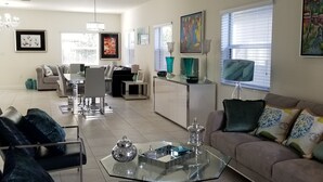 A modern living room with a glass coffee table, a sofa with decorative pillows, and a dining area with a white table and chairs. - Comfort, Serenity, Relaxation Vacation Home located in Homestead, Florida. (Homestead)