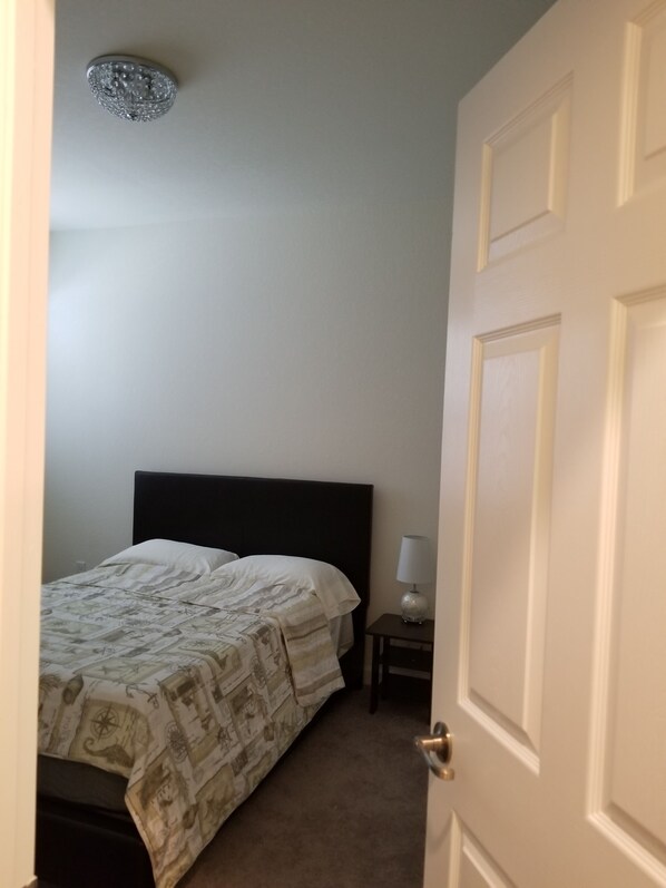 A bedroom with a bed, a bedside table with a lamp, and a door. - Comfort, Serenity, Relaxation Vacation Home located in Homestead, Florida. (Homestead)