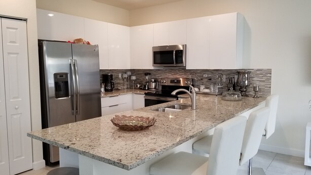 A modern kitchen with white cabinets, stainless steel appliances, a granite countertop, and a central island with bar stools. - Comfort, Serenity, Relaxation Vacation Home located in Homestead, Florida. (Homestead)