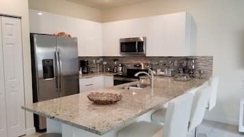 A modern kitchen with white cabinets, stainless steel appliances, a granite countertop, and bar stools.
