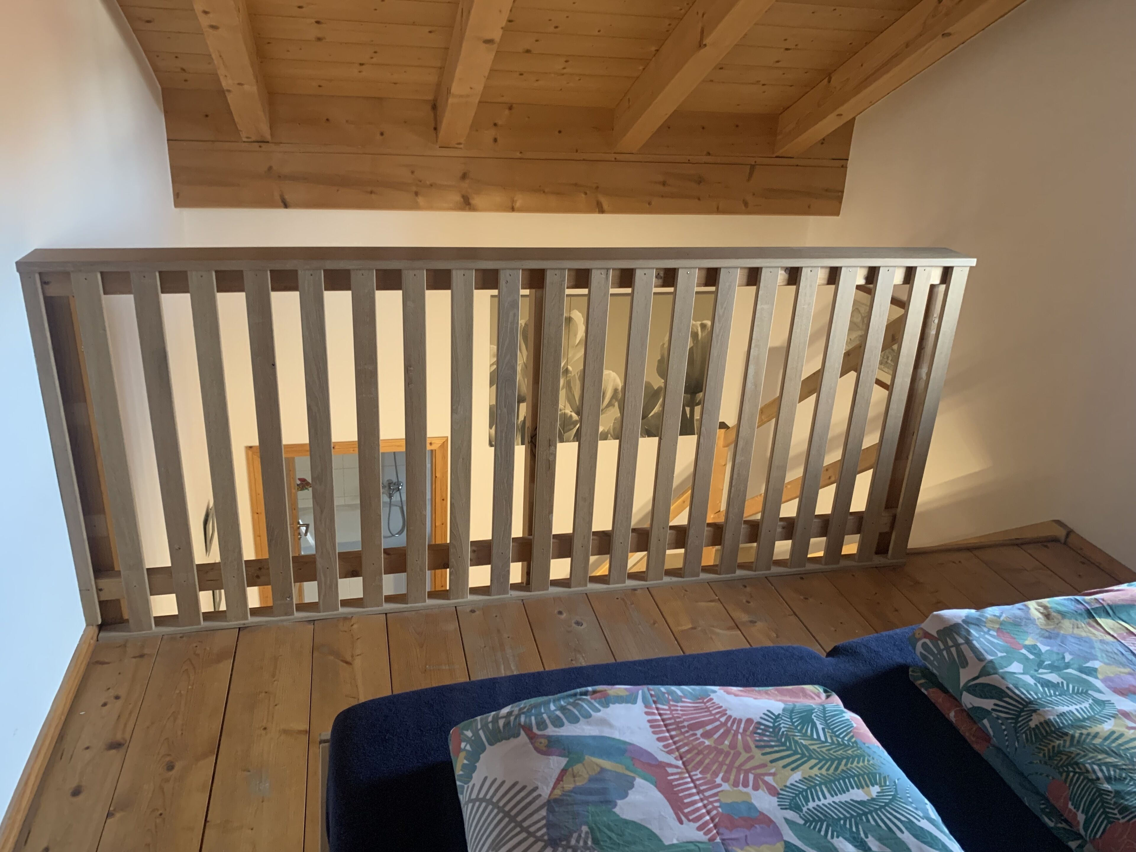 Une terrasse en bois avec une rambarde, une salle de bain avec douche et un lit recouvert d’une courtepointe aux motifs floraux colorés.