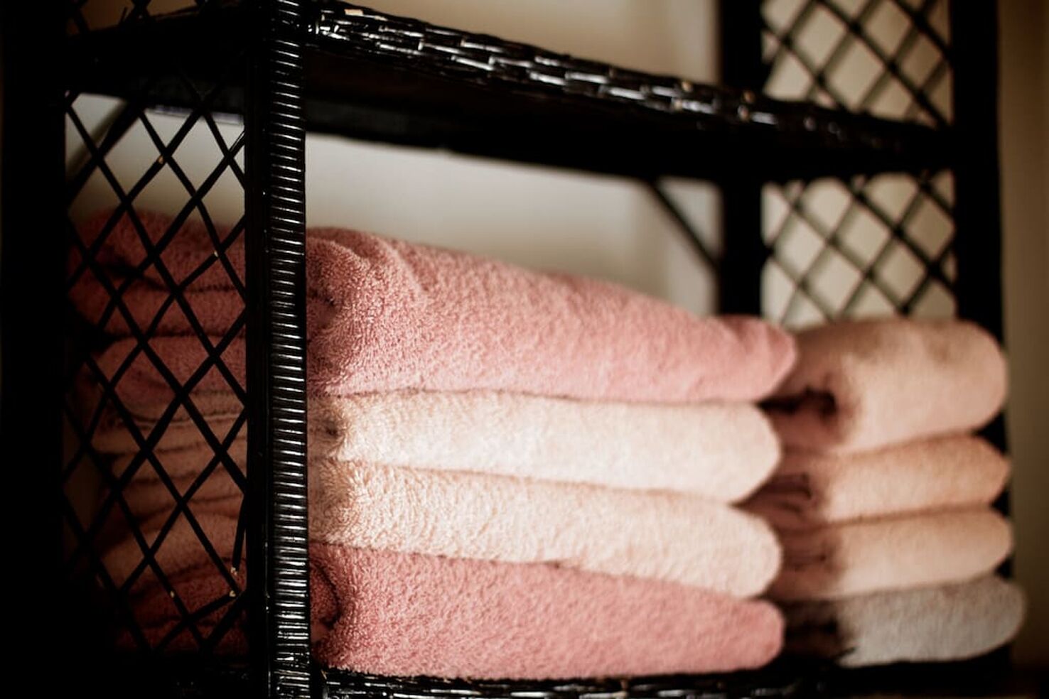 Un présentoir métallique noir sur lequel sont pliés des serviettes dans des tons de rose et de beige.