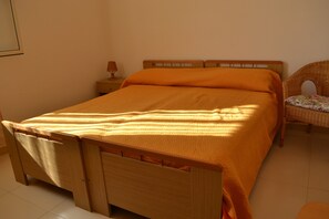 Un lit simple avec un cadre en bois et une couvre-lit orange, dans une pièce dont le sol est carrelé.