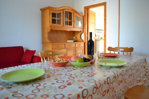 Un coin repas avec une table dressée pour deux personnes, un buffet en bois et une cuisine visible à travers une porte ouverte.