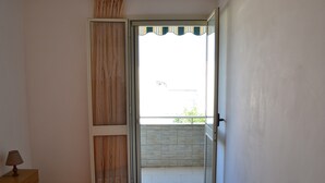 Camera da letto con un letto, un comodino, una lampada e una porta scorrevole in vetro che dà su un balcone.