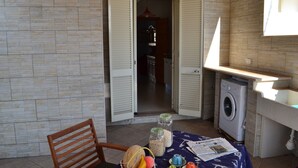 Una stanza modesta con un tavolo, una sedia, una lavatrice e una porta che dà su un'altra stanza.