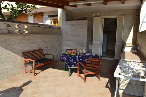 Un espace patio avec une table dressée pour les repas, deux chaises en bois et un banc.