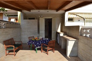 Une terrasse extérieure avec une table pour deux, un banc en bois et un petit coin cuisine.