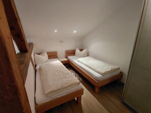 A small, well-lit room with two single beds, wooden headboards, and a sloped ceiling.