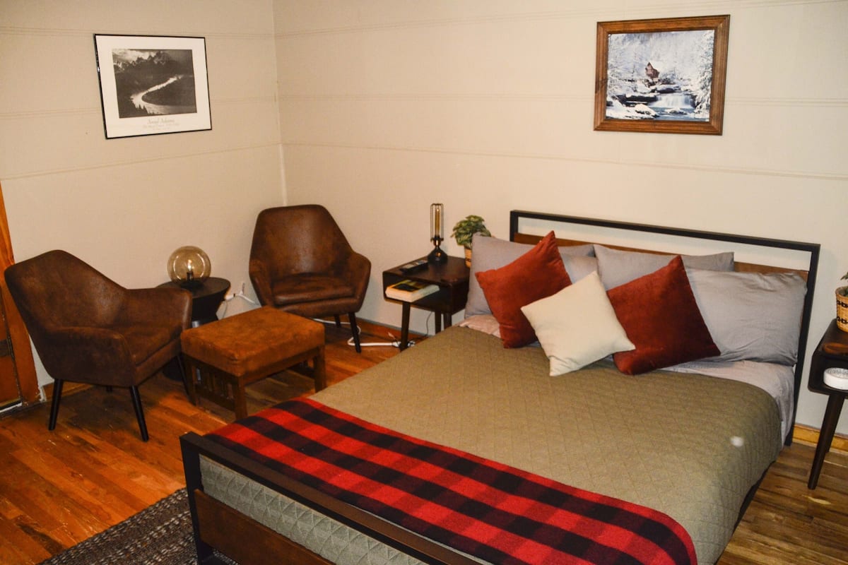 A bedroom with a bed, two chairs, a nightstand, and a lamp.