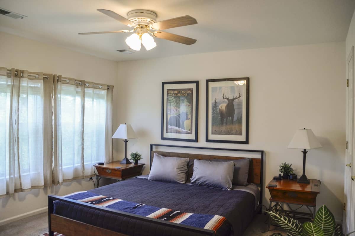 A bedroom with a bed, two nightstands, a ceiling fan, and two framed pictures on the wall.