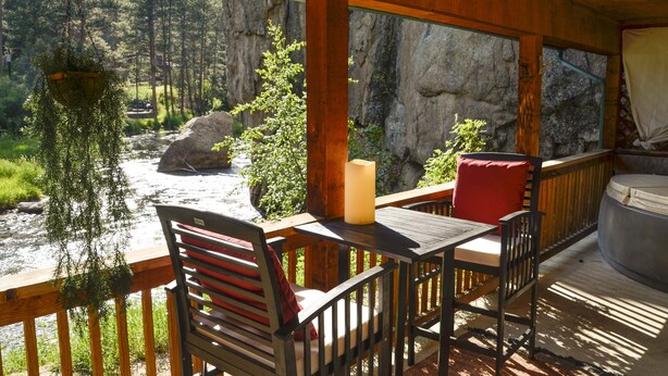 A wooden deck with a table and chairs, overlooking a river and forest. - The Woolly Bugger Inn (Drake)