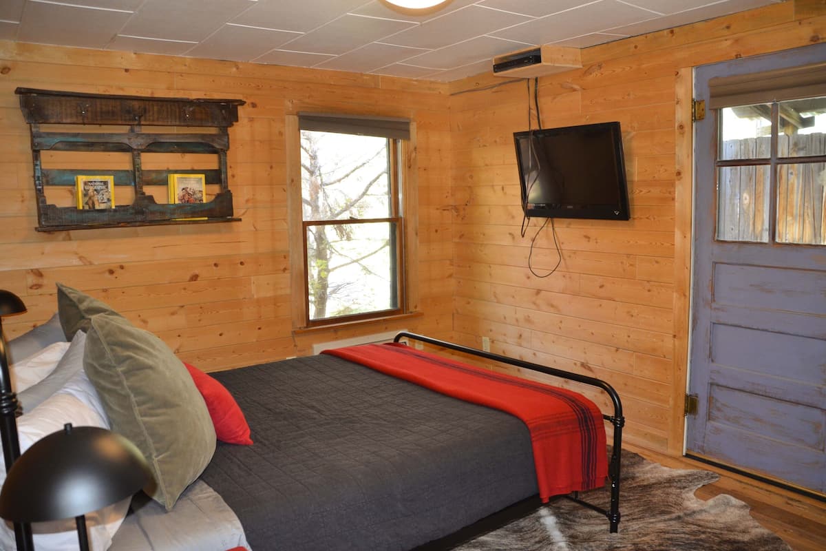 A wooden-paneled room with a bed, a mounted TV, and a window.